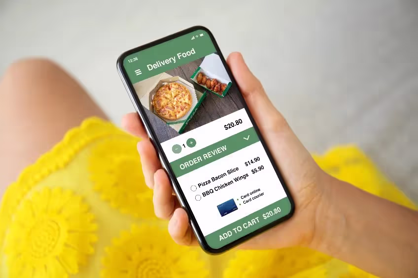 Hand holding smartphone displaying a food delivery app with pizza and chicken wings in the order review.